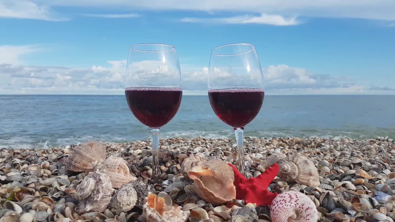 两杯盛满干红葡萄酒的杯子放在贝壳里，映衬着大海和蓝天白云视频素材