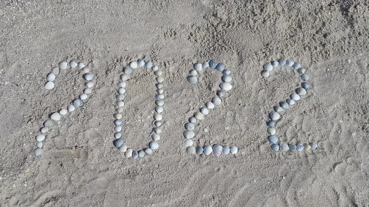 女孩的手从海边的贝壳上摊开数字“2022”视频素材