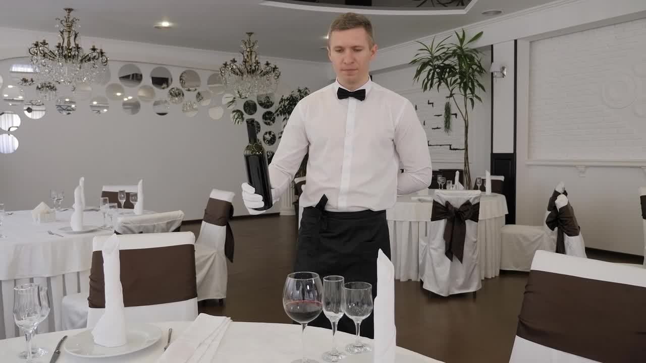 在一家餐馆里，一位戴着白手套的男侍者正在把红酒倒进杯子里。视频下载