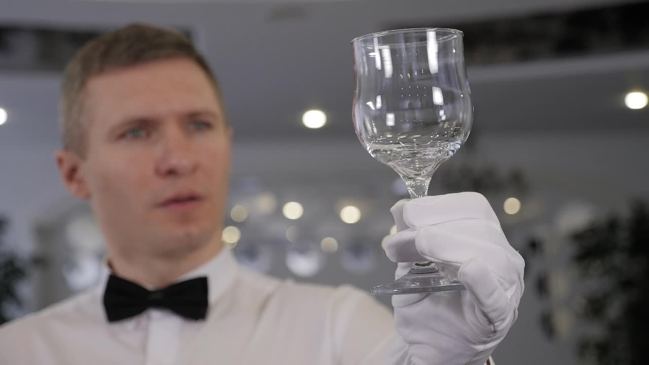 一名穿着白衬衫、戴着白手套的服务员用白毛巾擦拭酒杯视频下载