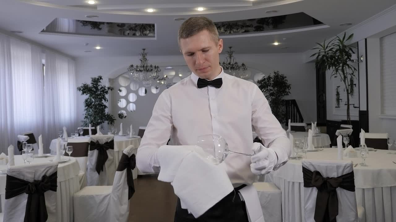 在餐厅里，一个戴白手套的服务员用毛巾擦拭杯子。视频下载