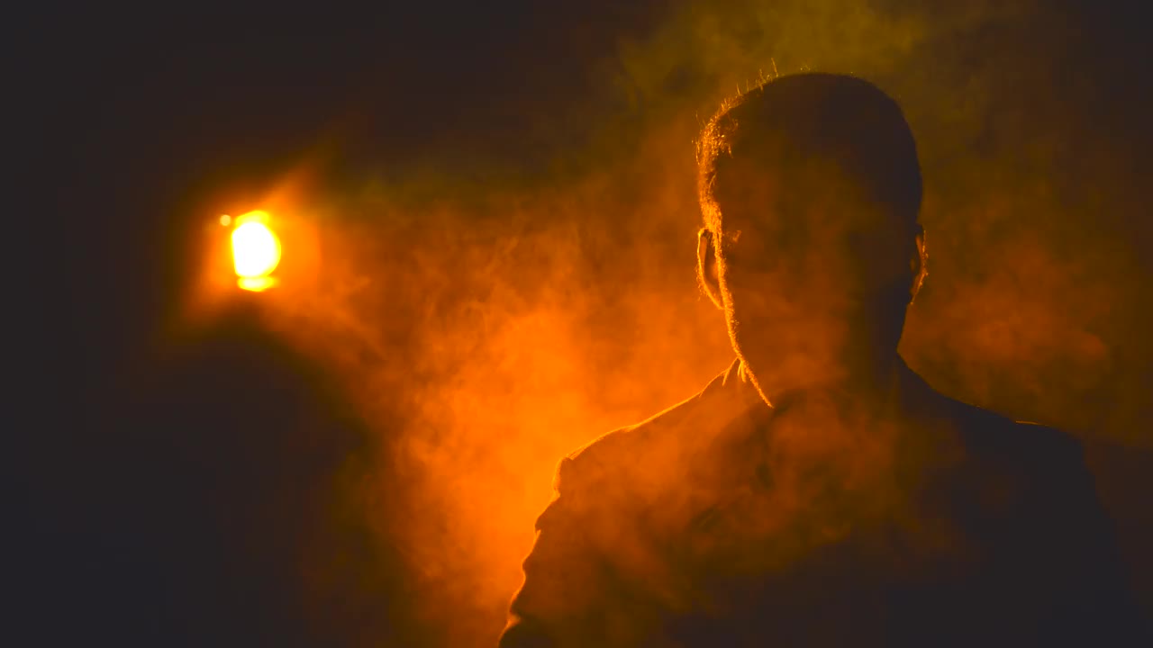 4k特写视频，男性的脸在阴影和烟雾和橙色的光的背景。视频素材