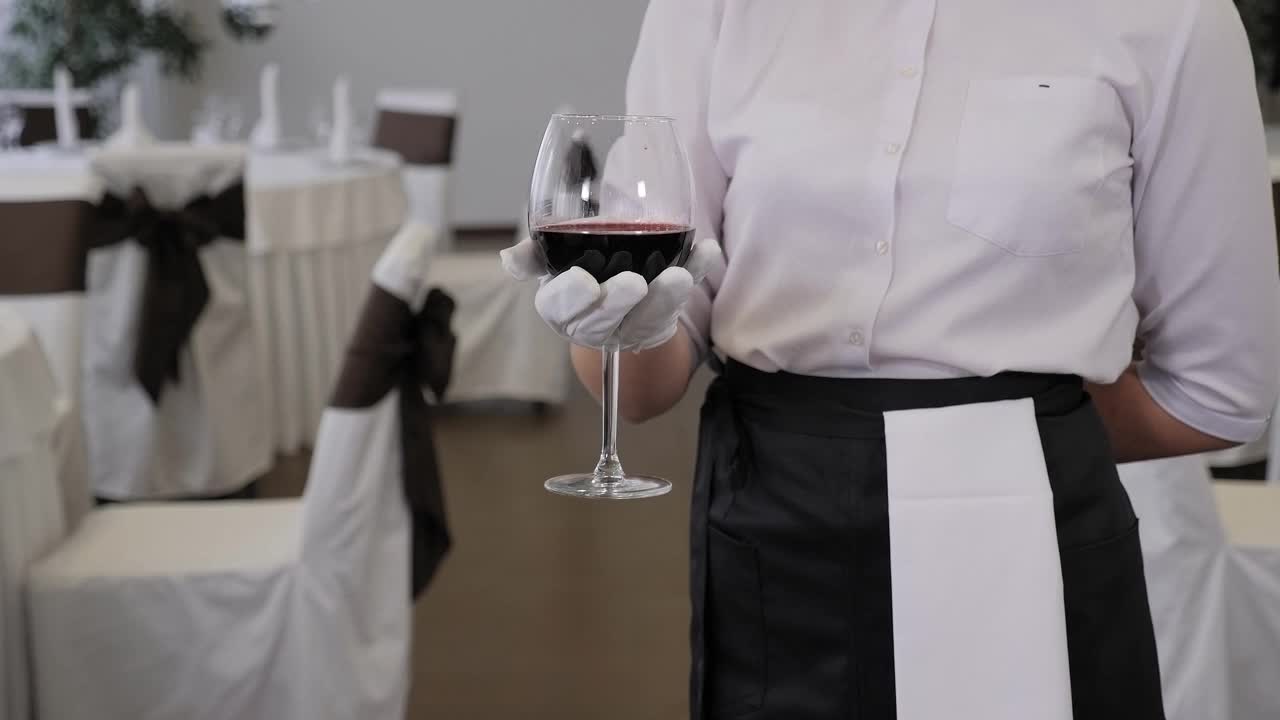 一个年轻的女性侍酒师举着一杯红酒的特写。视频下载