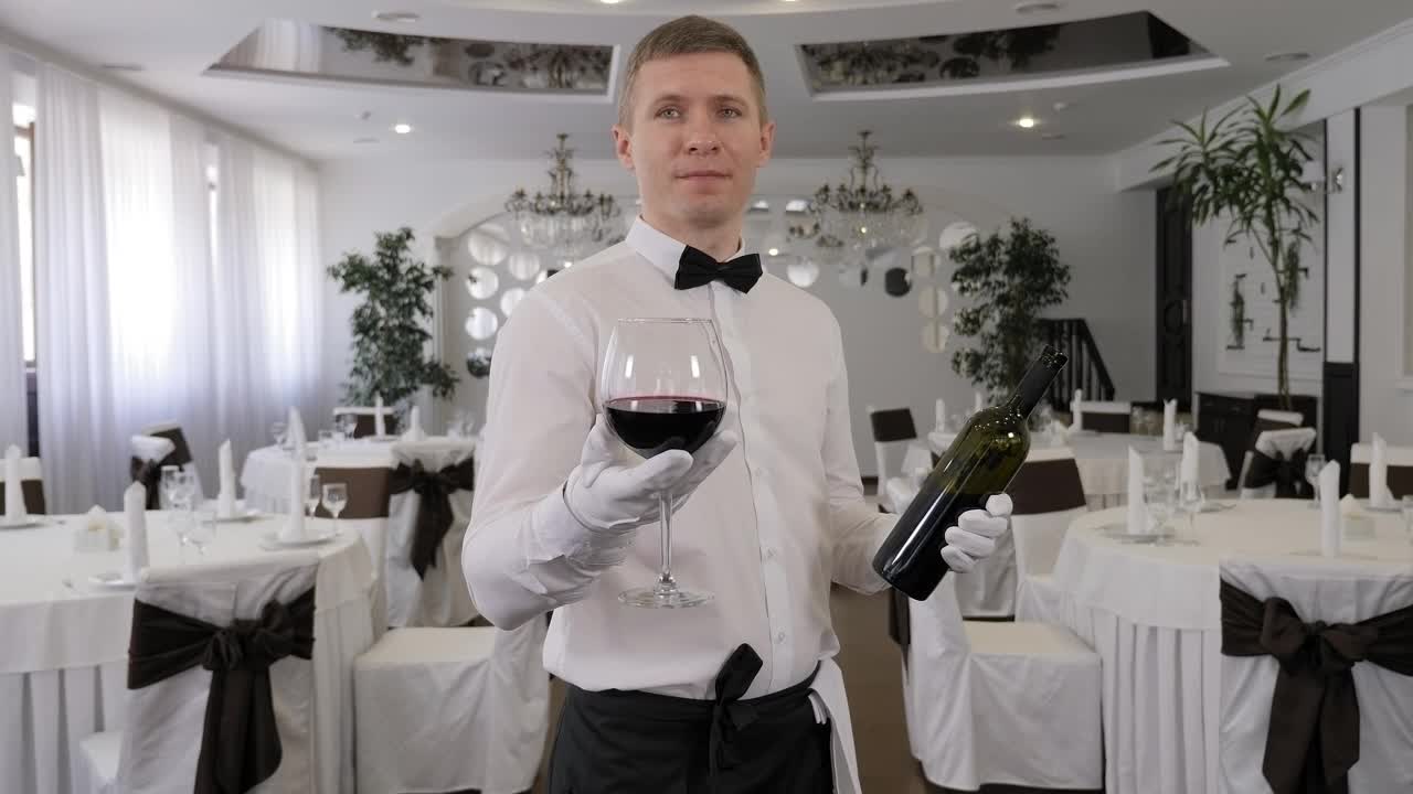 在一家餐馆里，一名男服务员手里拿着一杯红酒。视频下载