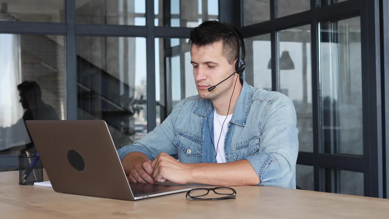 交谈，会议在线或电子教育，客户支持的概念。微笑的年轻白人男子戴着耳机使用笔记本电脑进行视频通话视频下载