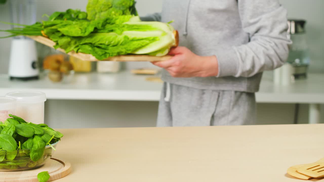 将带有新鲜绿叶蔬菜的切菜板放在桌子上。准备洗净的大葱、黄瓜、花椰菜、生菜、菠菜等烹调健康食品。素食餐视频素材