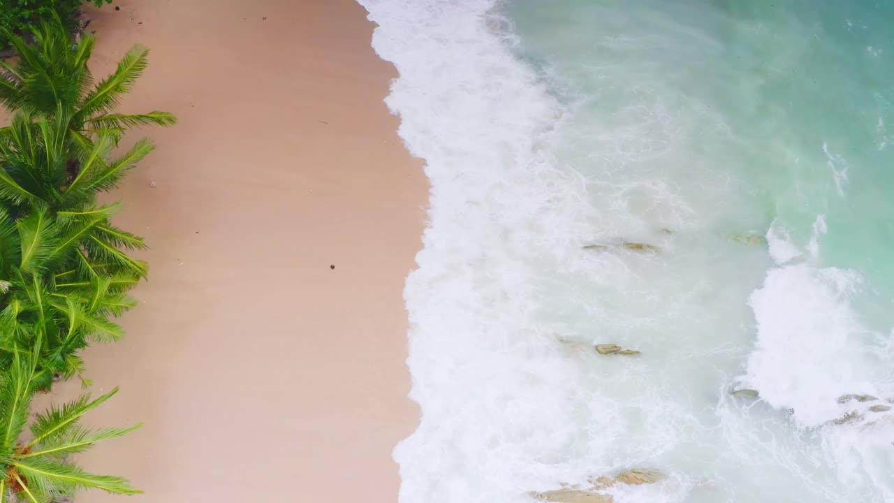 4K无人机从上到下鸟瞰大海，蓝色的海浪拍打在岩石和沙子上。美丽的海水海浪来到海滩视频素材