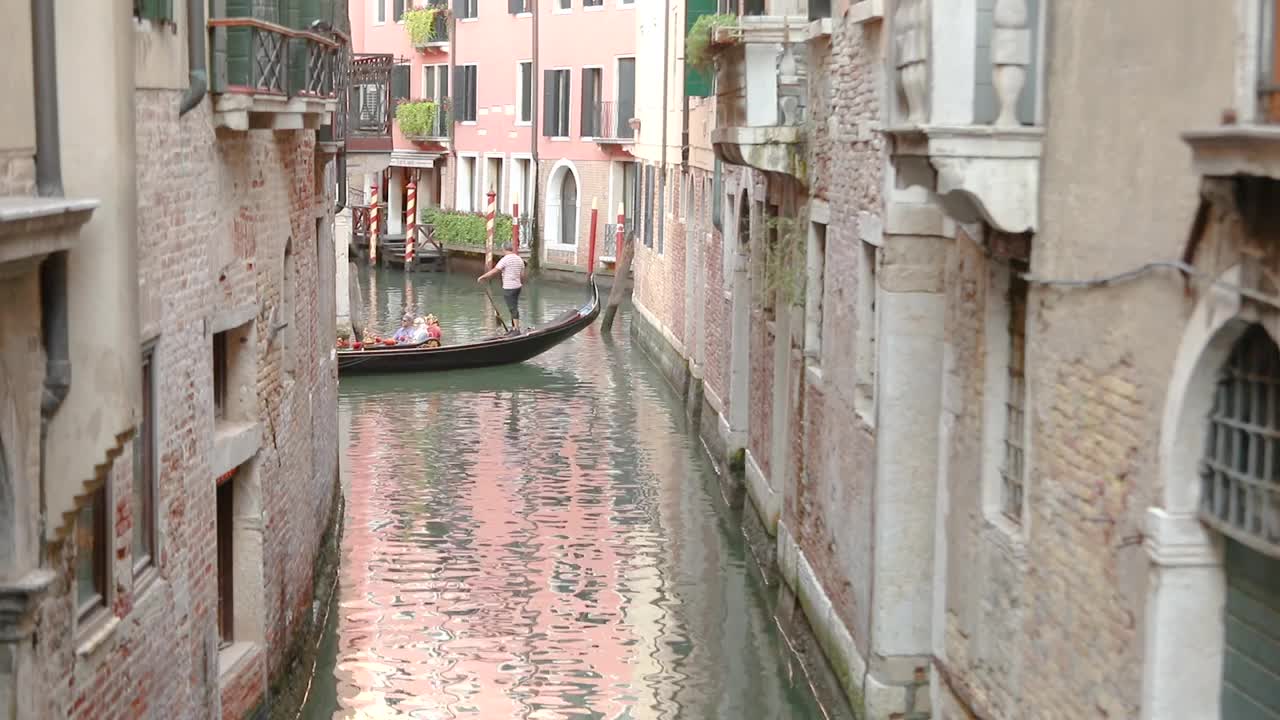 在威尼斯一条美丽狭窄的运河里，游人乘坐平底船。美丽的威尼斯运河。威尼斯，意大利。威尼斯浪漫的地方视频素材