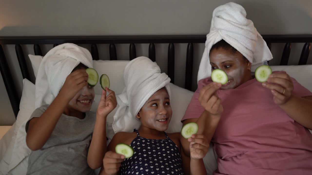 母亲和女儿在床上用黄瓜片敷在眼睛上做皮肤护理视频下载