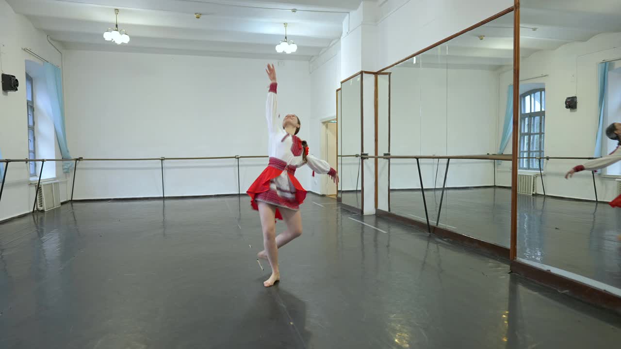 宽镜头苗条华丽的乌克兰年轻女子在民族服装纺纱在慢动作排练舞蹈在工作室。快乐美丽的白人舞者在室内表演民间舞蹈。视频素材