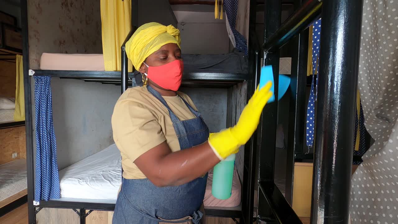 一名非洲妇女用清洁海绵和酒精消毒液喷雾清洁宿舍房间的4K视频视频下载