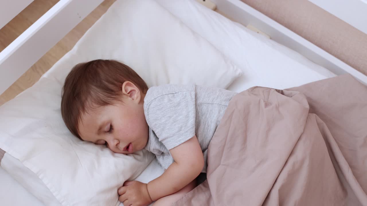 安静可爱的蹒跚学步的婴儿睡在他的床上。睡着的孩子的概念。两岁的孩子睡在家里。视频下载