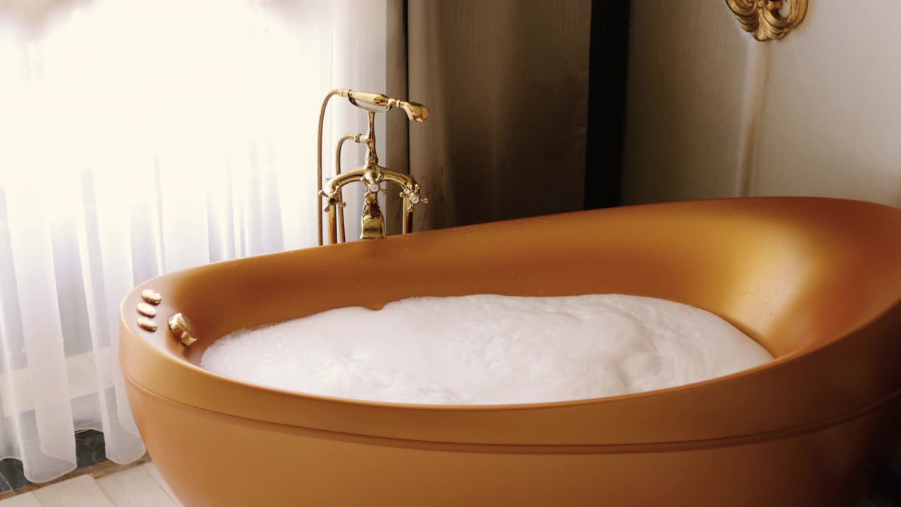 浴缸里有白色的软泡沫。金色浴盆，豪华酒店客房，酒店套房视频下载