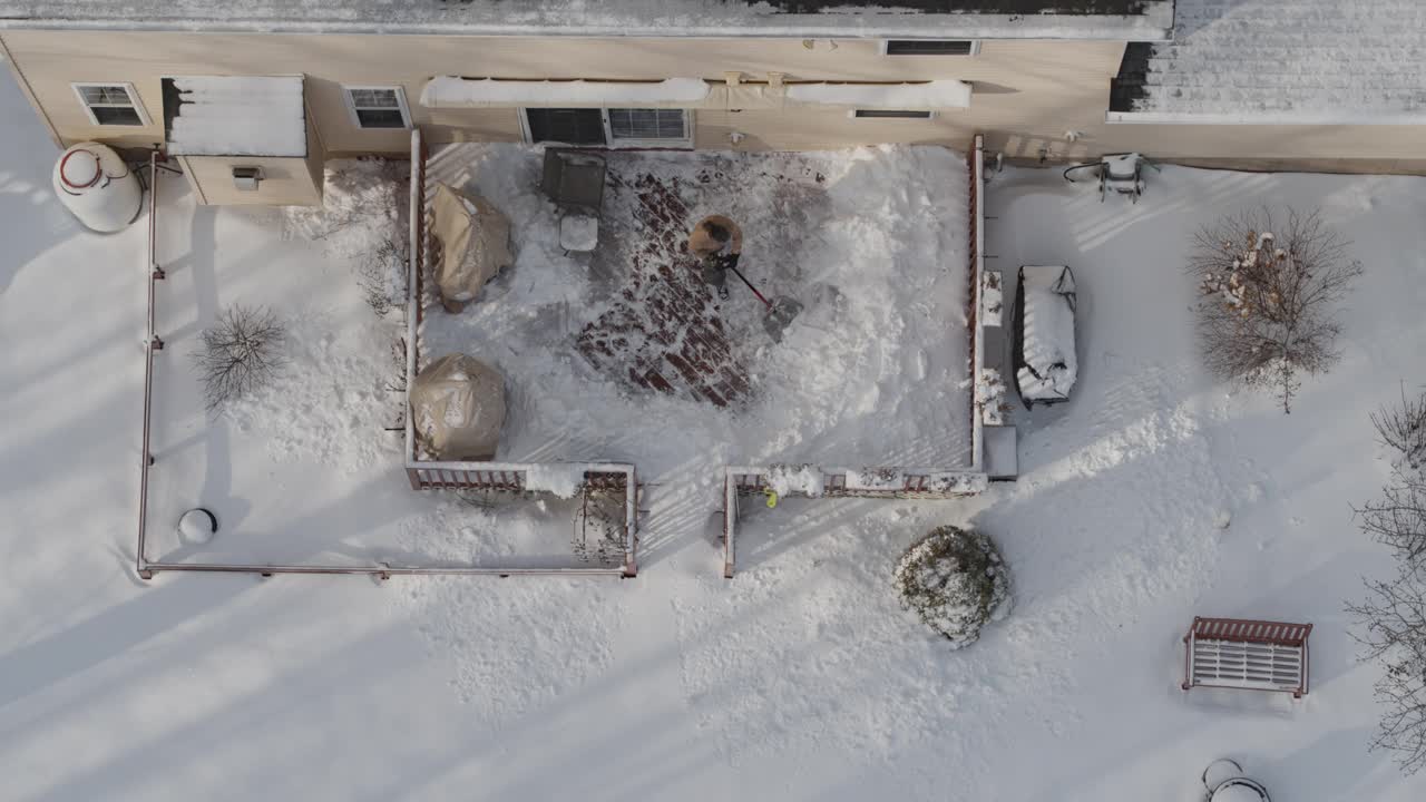 一个成年男子在一场冬季降雪后用铲子清理门廊上的积雪。鸟瞰图正上方无人机视频。视频下载