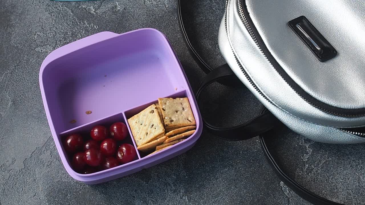 女人从背包里拿出午餐盒，里面有三明治、饼干和樱桃。零食的概念在学校，办公室，家庭之外。视频素材