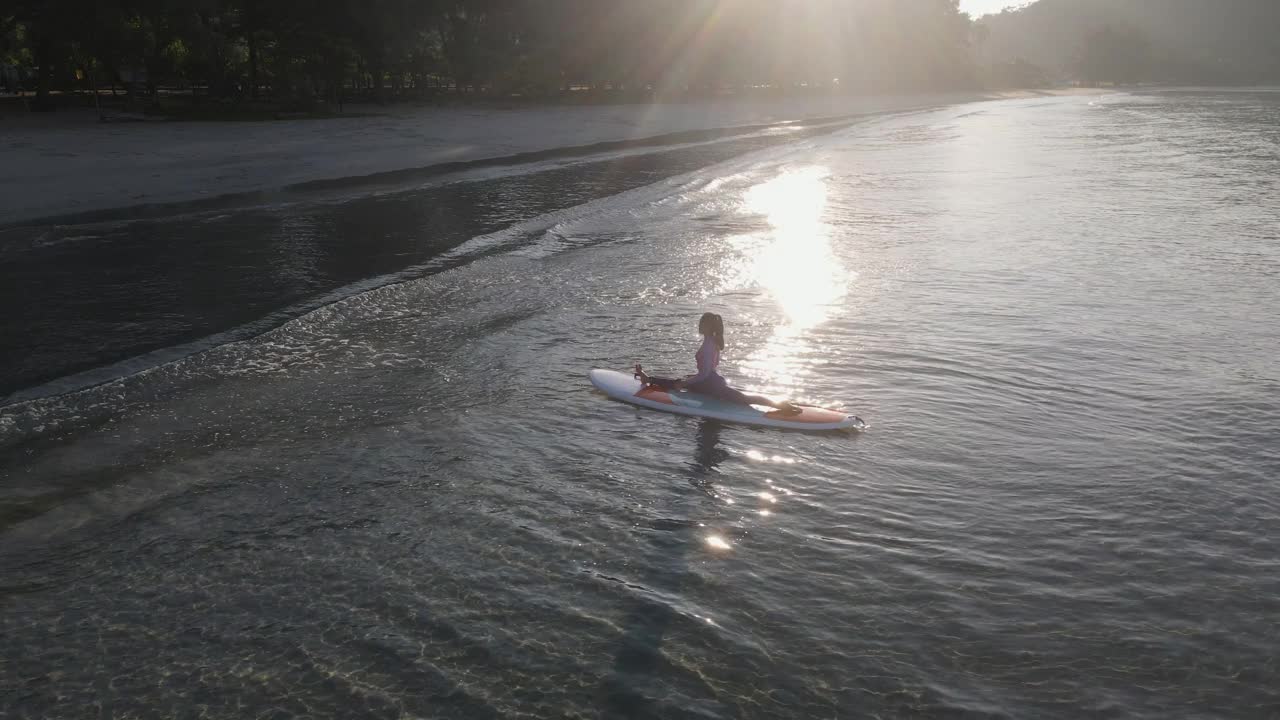 在阳光明媚的夏日，在海洋中，积极的女性瑜伽练习站起来划水板。视频下载