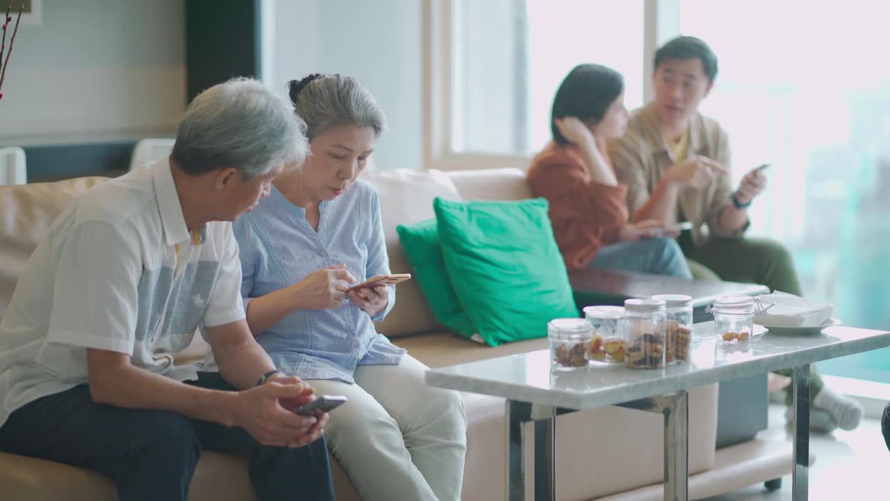 亚洲华人祖父母和年轻夫妇在客厅用手机浏览互联网视频素材