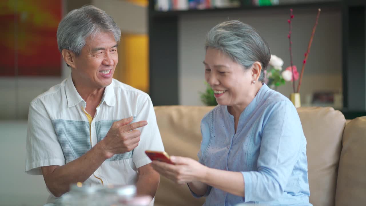 快乐的亚洲华人祖父母使用电话，在客厅愉快地交谈视频素材