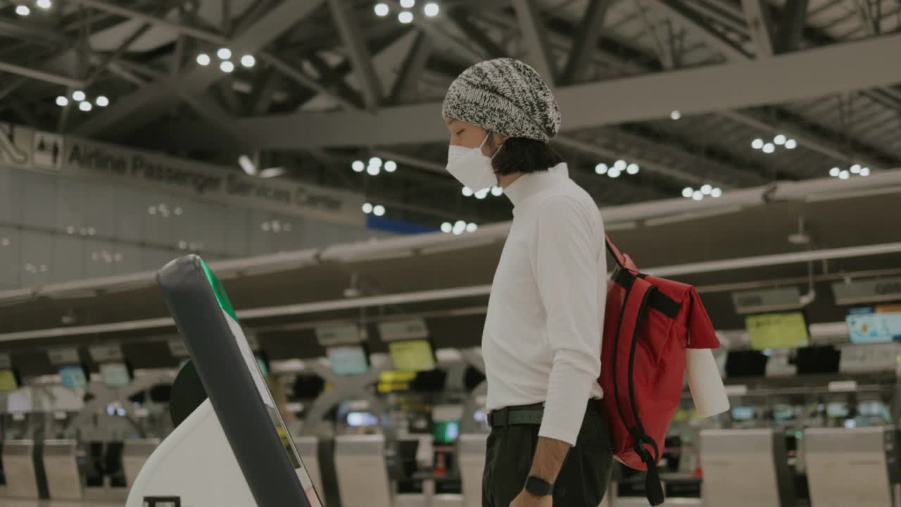 亚洲青年男子戴着无檐便帽和防护口罩在登机前进行自我登记视频下载