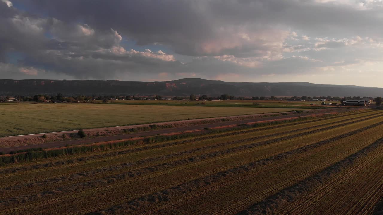在科罗拉多州西部的夏季黄昏，无人机飞过一个新割的干草田，在Fruita科罗拉多附近的标志性科罗拉多国家纪念碑的远处视频下载