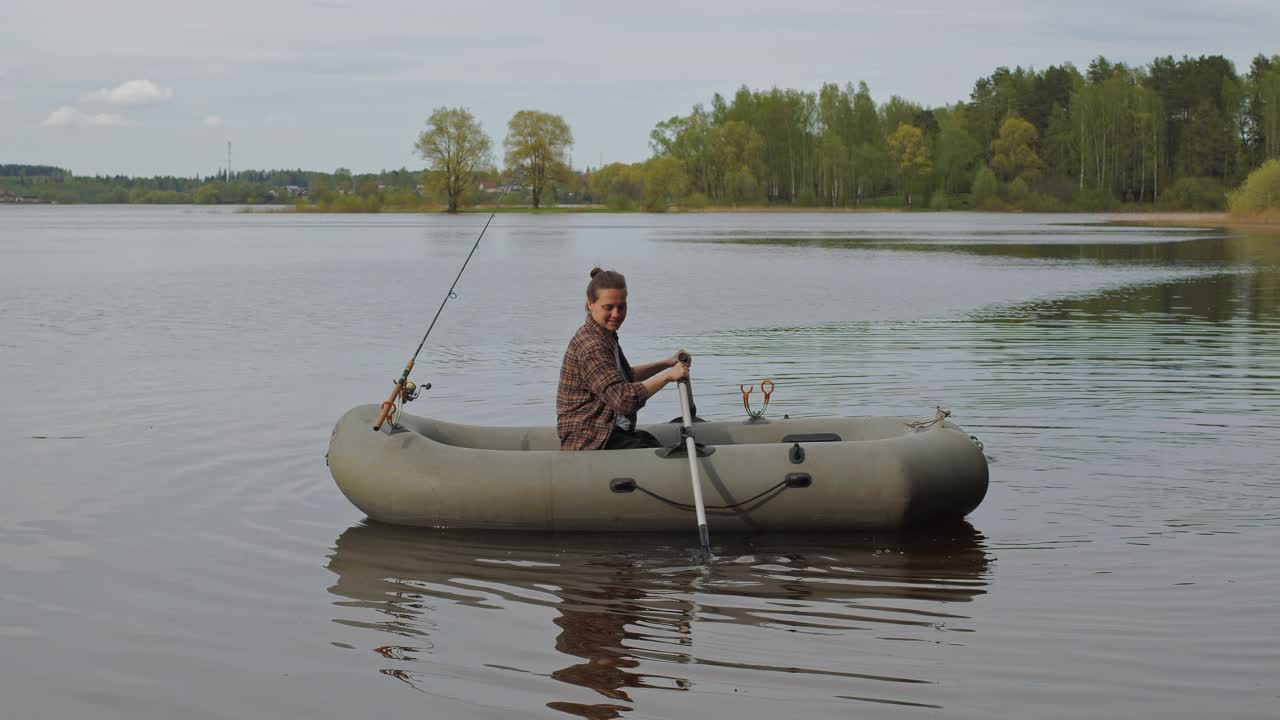 美丽的电影拍摄。少女渔夫在湖中划着充气船。视频下载