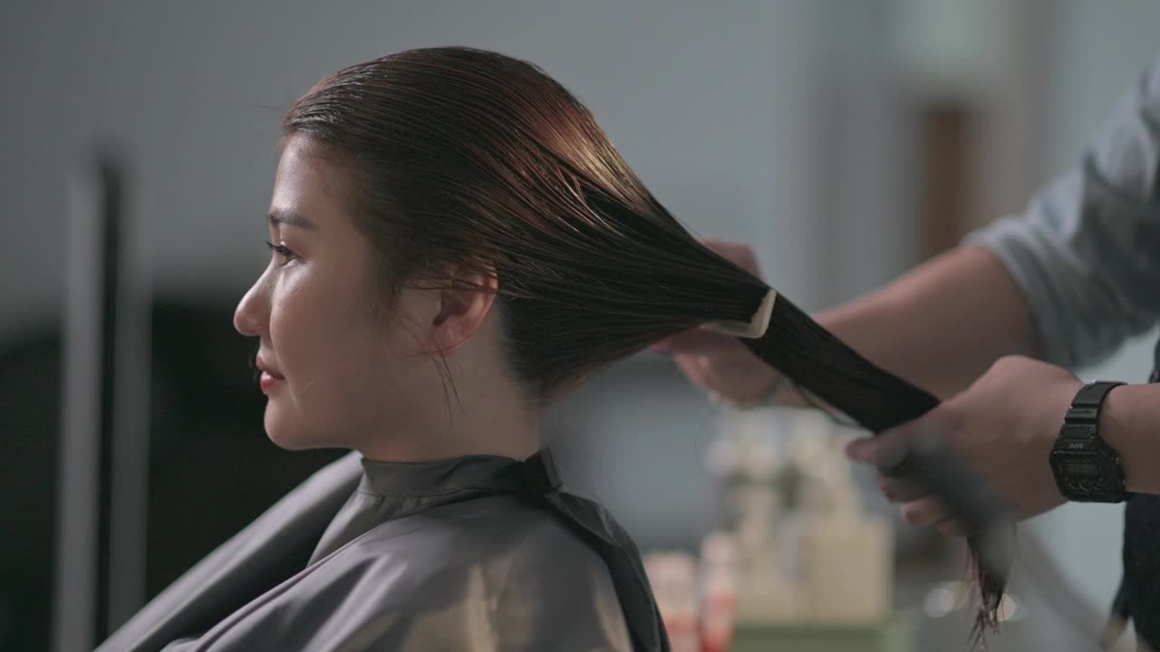 美发沙龙亚洲华人女性发型师在美发沙龙为她的顾客剪发梳理湿长发视频素材