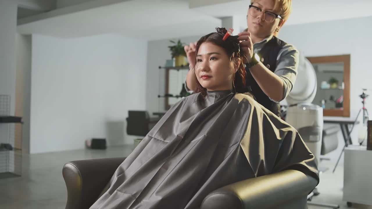 慢动作美发沙龙亚洲华裔女性发型师在美发沙龙为她的顾客剪发梳理湿长发视频素材