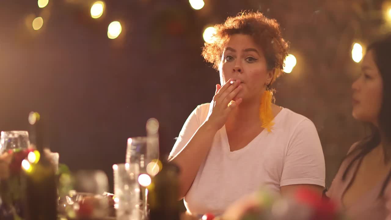 年轻女子吸烟时，享受晚餐派对与她的朋友在后院视频下载