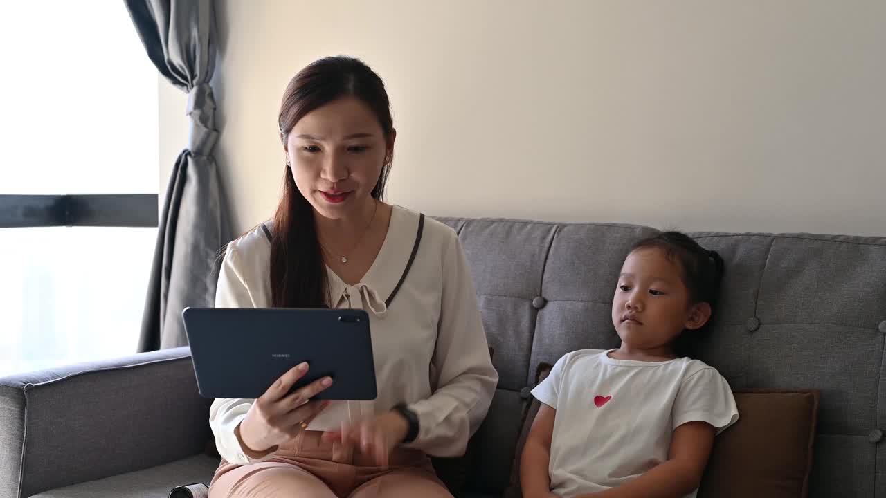 一位亚裔母亲和她的女儿在家里与一位儿科医生进行视频通话视频下载
