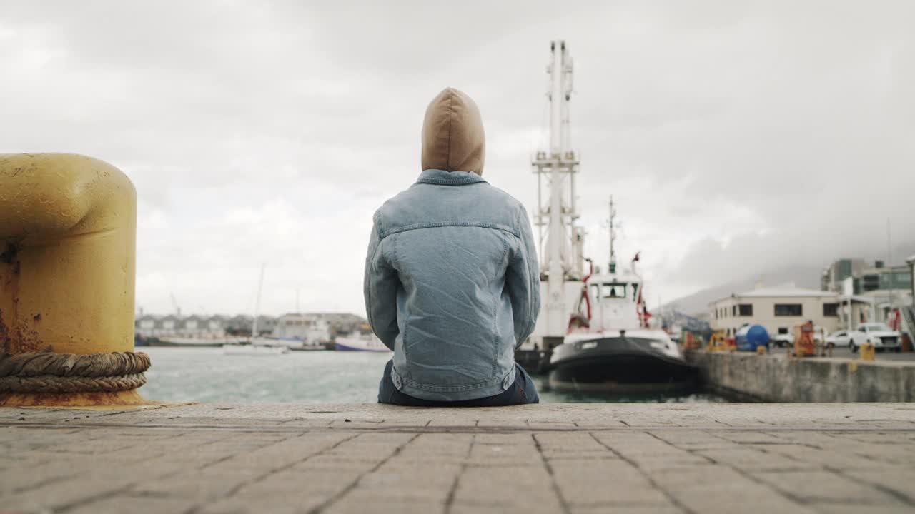 一个年轻人坐在港口的码头上欣赏风景的4k视频片段视频下载