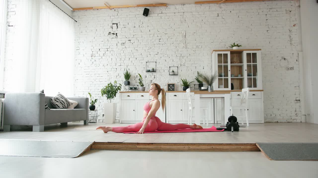 混合种族的金发女人在家里做瑜伽健身运动的扭曲和灵活性视频下载