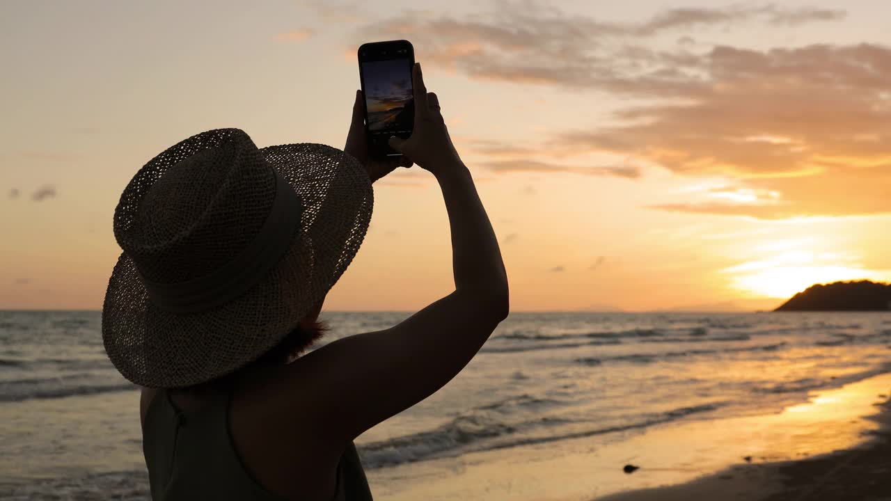 快乐的年轻女子散步和拍照的海边美丽的日落剪影视频素材
