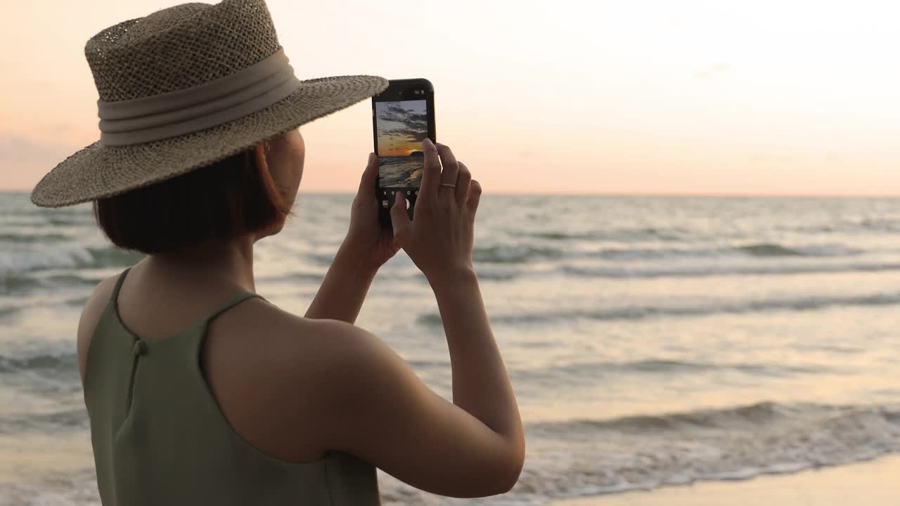 快乐的年轻女子散步和拍照的海边美丽的日落剪影视频下载