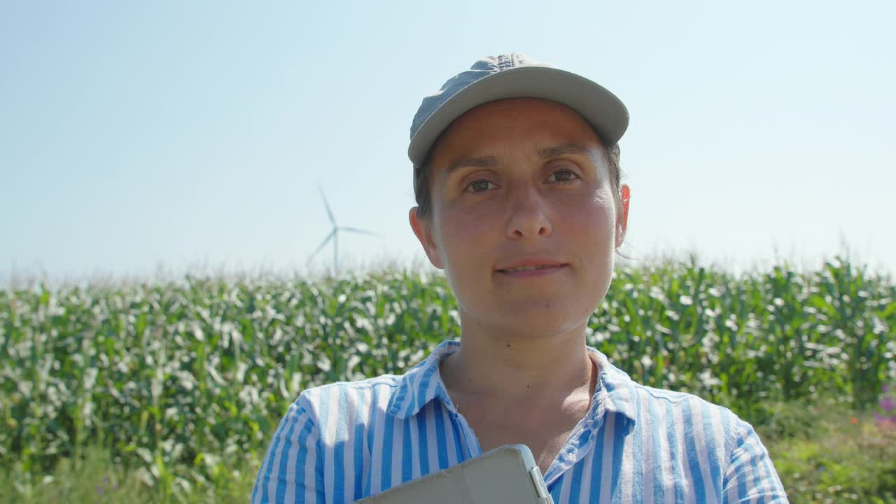 这是一幅农妇在耕种的玉米地里的肖像，后面有风力发电机。农业、可持续性和环境保护。视频下载