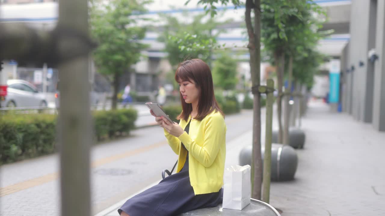 女商人穿着黄色休闲羊毛衫在城市里看手机短信视频下载