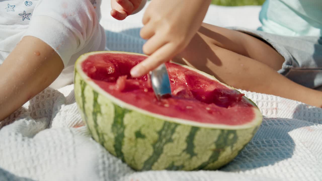 特写的孩子们用勺子在户外拿新鲜的西瓜水果视频下载