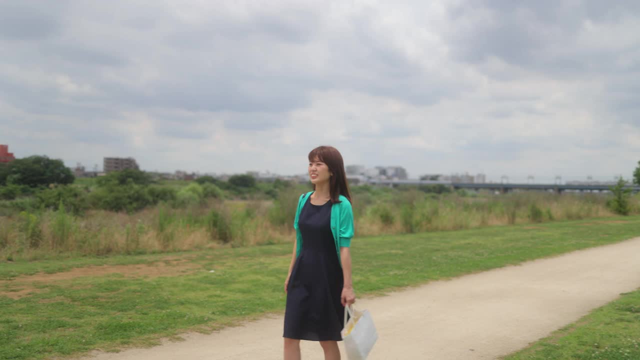 穿着绿色开襟羊毛衫的女人走在河岸上视频素材