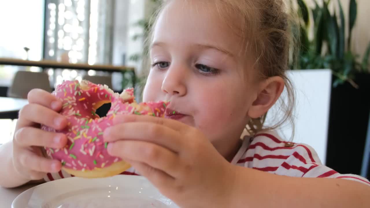 可爱的小女孩在吃粉色的甜甜圈视频素材