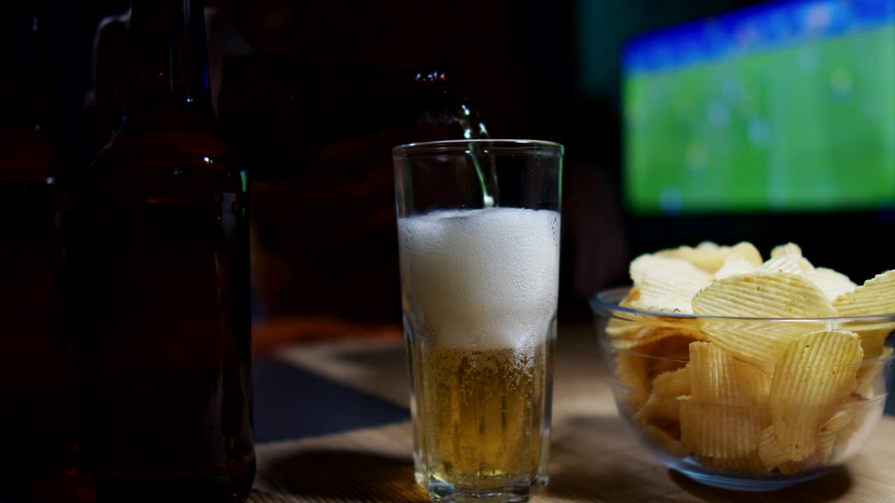 这个人正在看电视上的体育比赛，在家里喝啤酒吃薯片视频下载