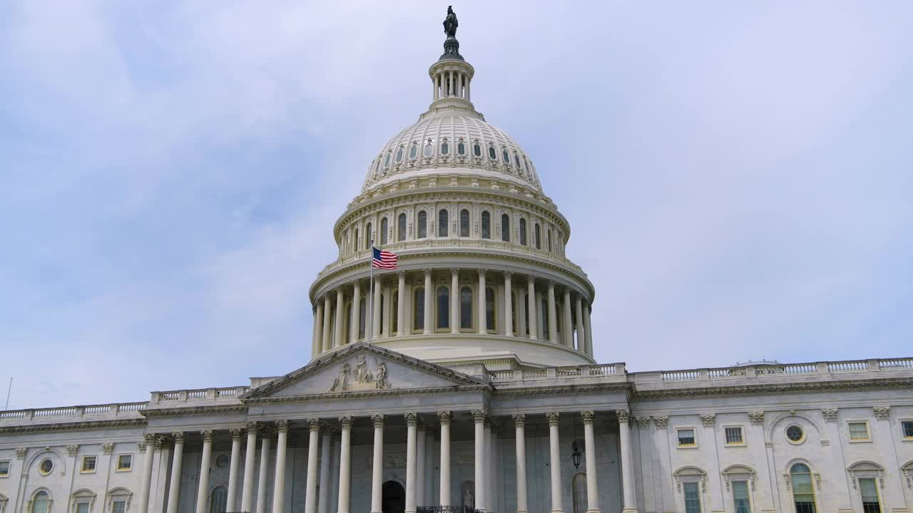 国会大厦——在一个阳光明媚的日子里，美国华盛顿特区，美国国会大厦东侧飘扬着一面美国国旗的特写。视频下载