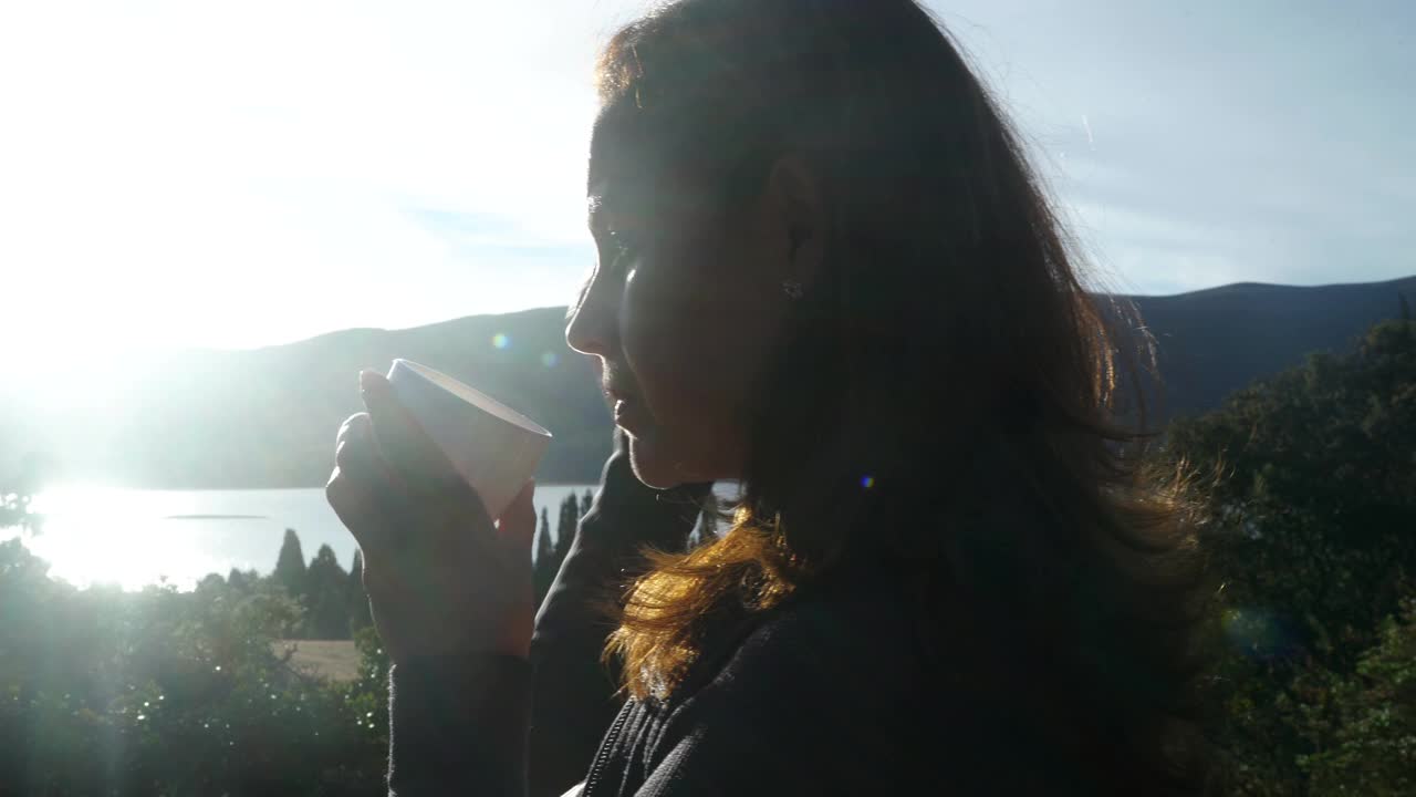 拉丁女人手里拿着一杯咖啡，欣赏森林里的日落视频素材