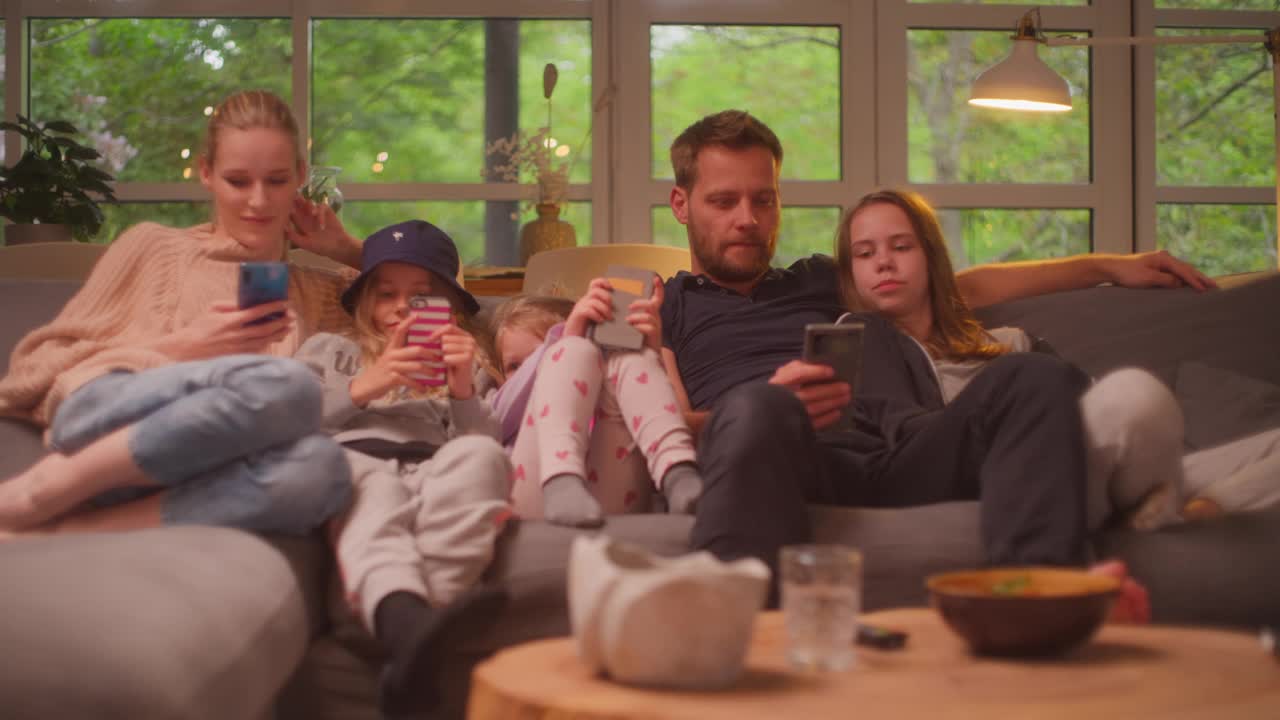 在家看电视。一家人和三个女儿在一起。在沙发上玩智能手机视频下载
