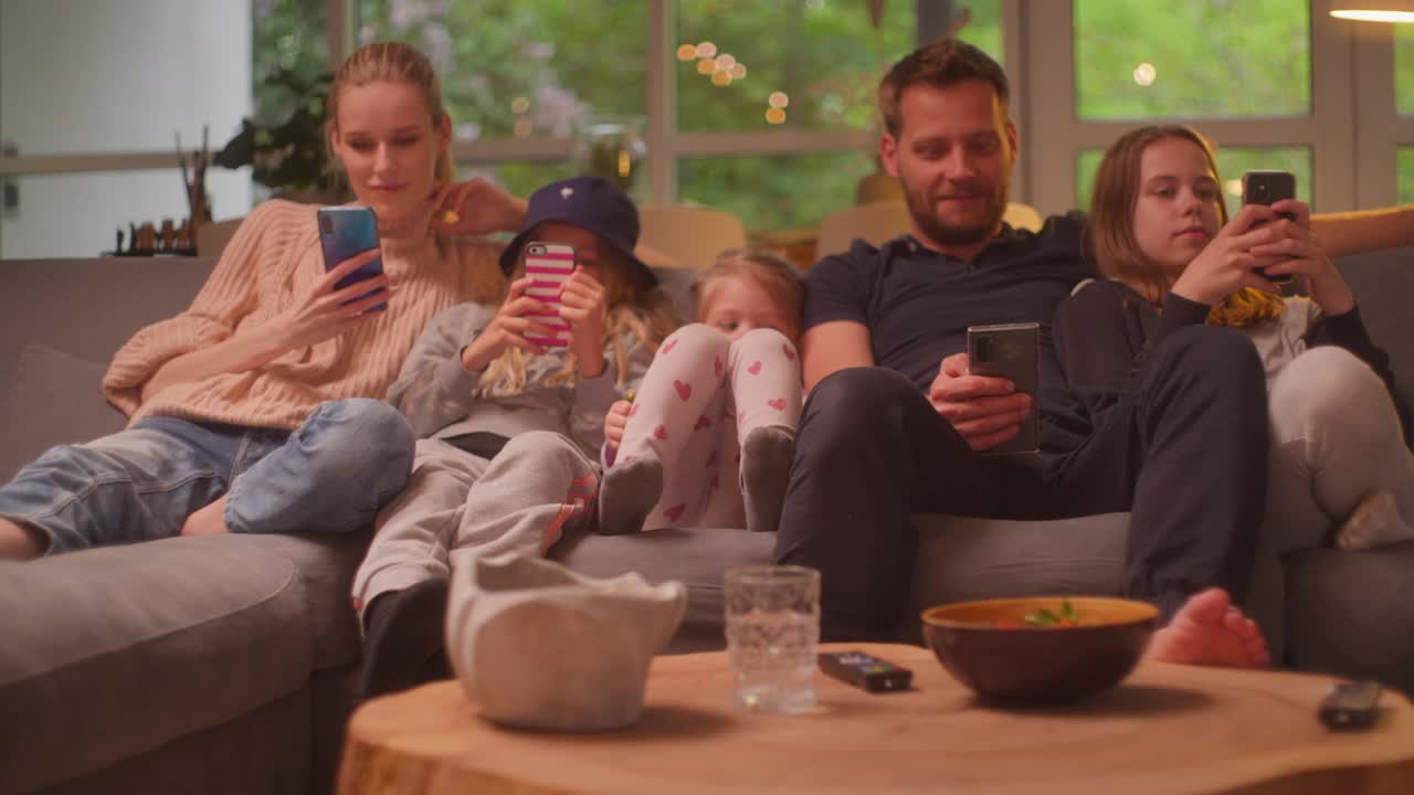 在家看电视。一家人和三个女儿在一起。在沙发上玩智能手机视频下载