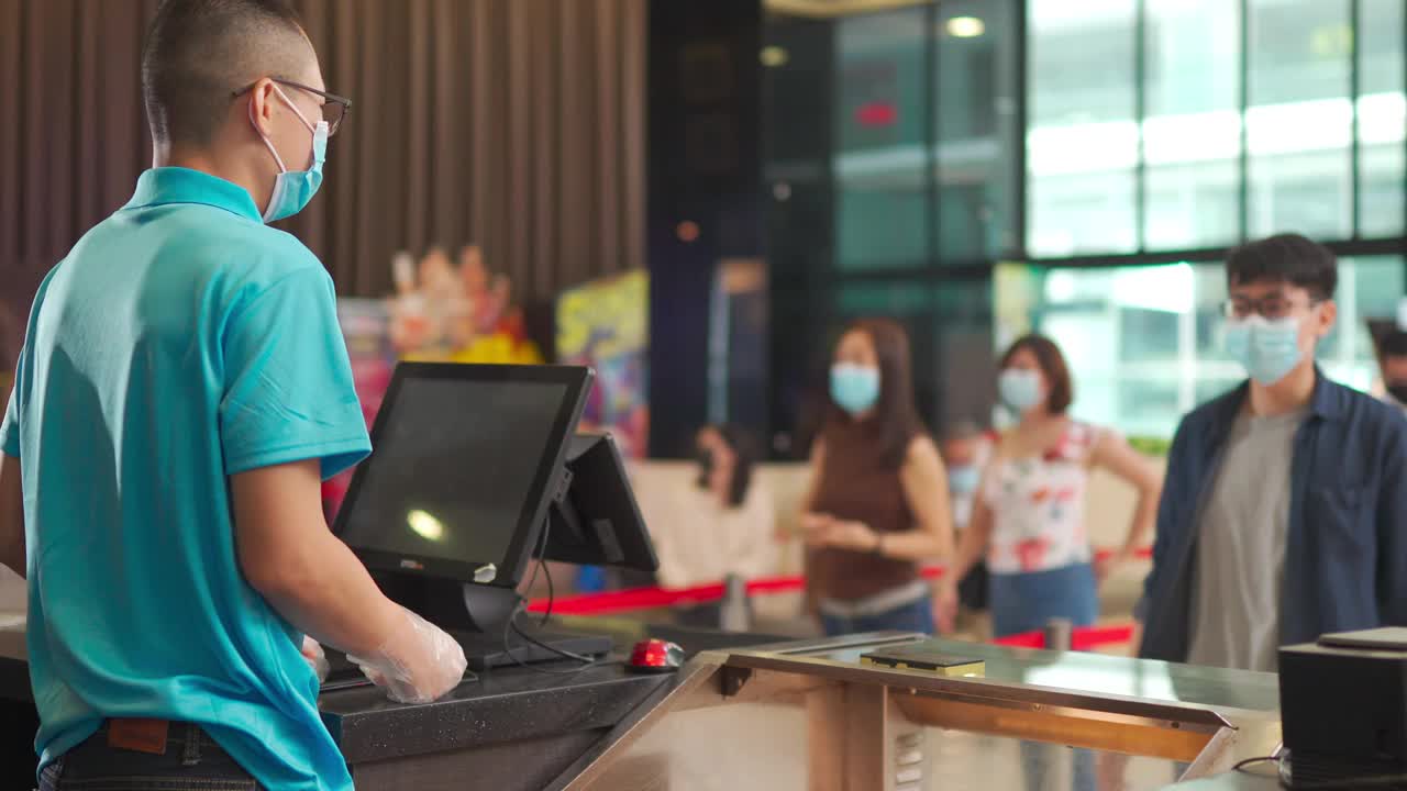 一名戴着口罩的亚洲华裔年轻人在电影院开映前在吧台点了爆米花矿泉水视频素材