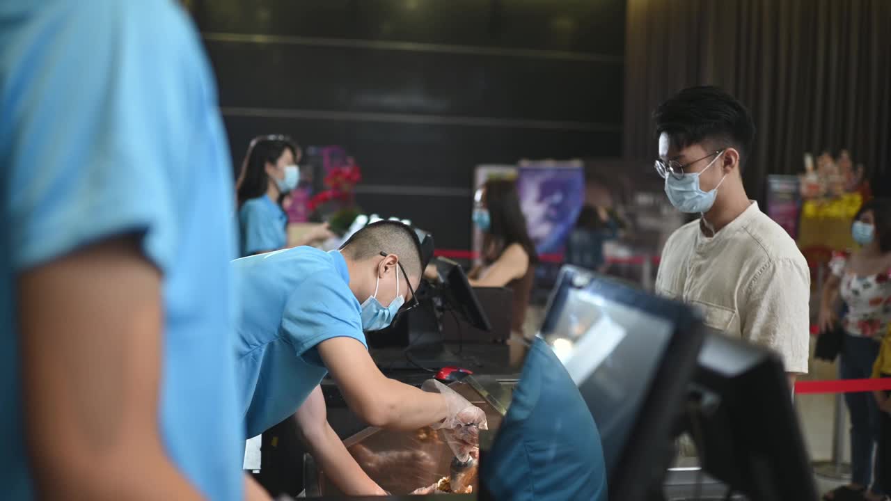 亚洲华人年轻人戴着面具在电影院放电影前买爆米花视频素材