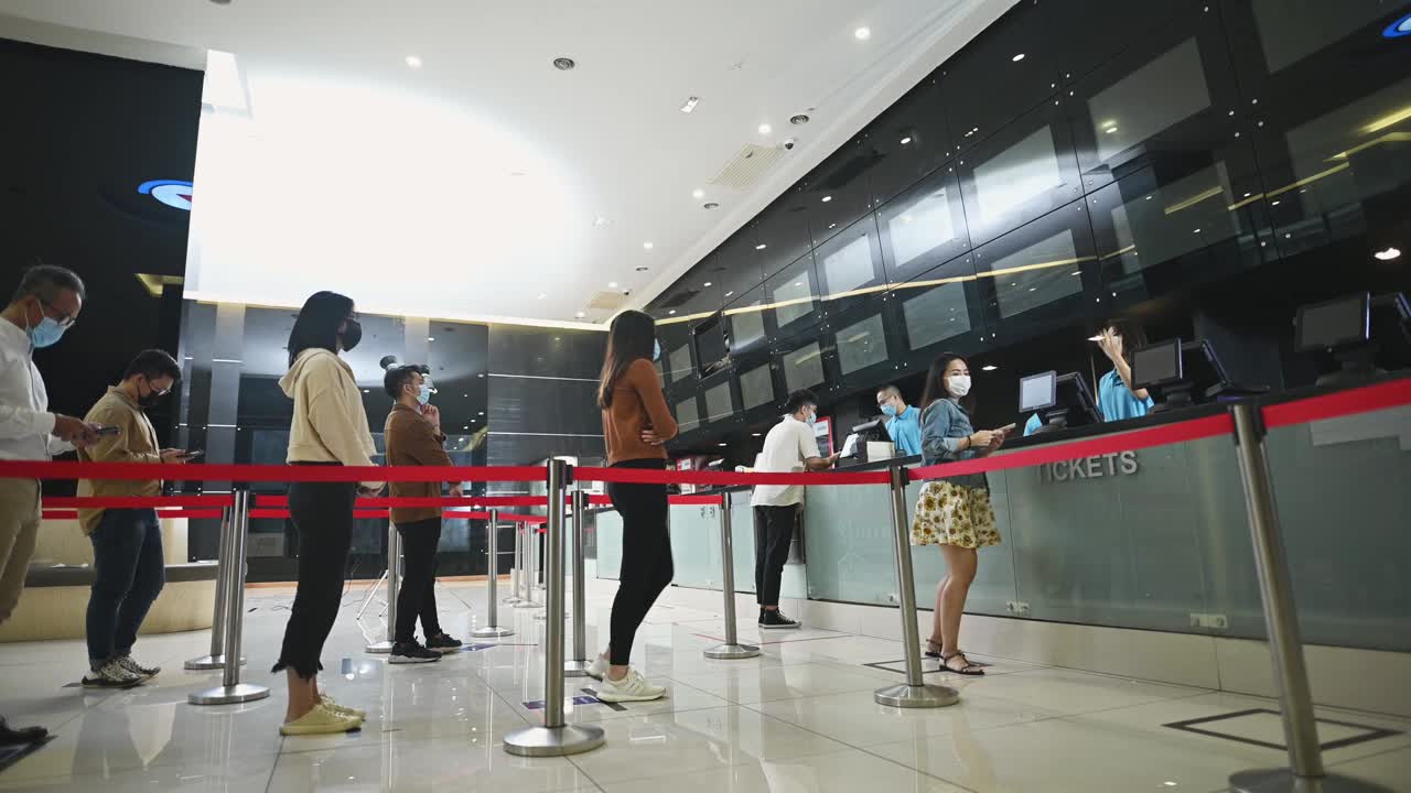低角度的亚洲华人观众在售票柜台前排队购买电影票和爆米花饮料，在电影院放映前进行非接触式支付视频素材