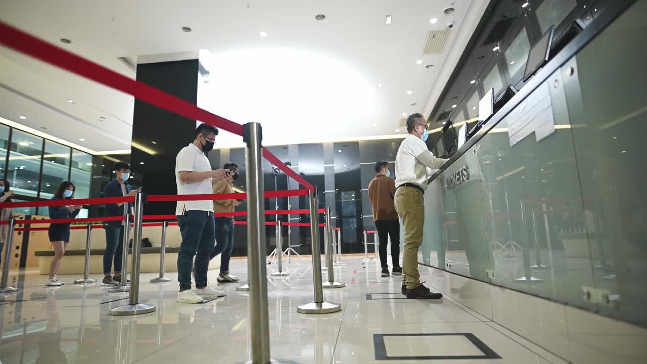 低角度的亚洲华人观众在售票柜台前排队购买电影票和爆米花饮料，在电影院放映前进行非接触式支付视频素材