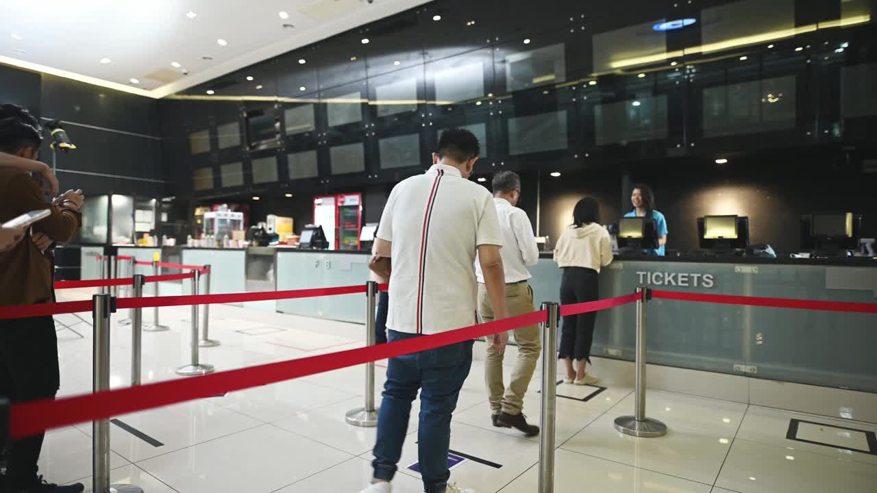 低角度观看亚洲华人观众在电影院售票柜台前排队购买电影票和爆米花饮料，在电影院放映前进行非接触式支付视频素材