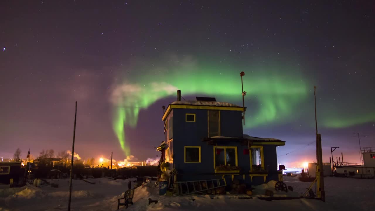 加拿大不列颠哥伦比亚省，日落时天空中的北极光从蓝色房子的烟囱中释放蒸汽的延时拍摄视频素材