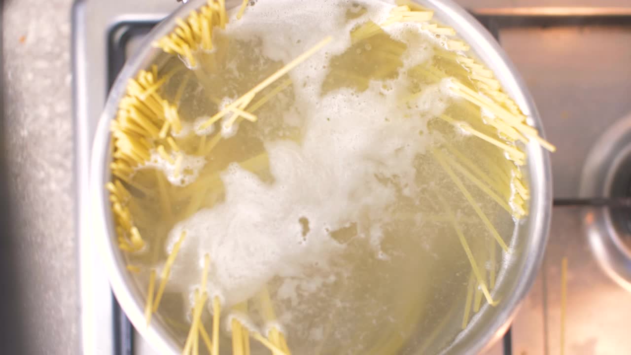 俯视图上的银锅的沸水在厨房炉子上。厨师添加正宗的意大利细面条视频素材